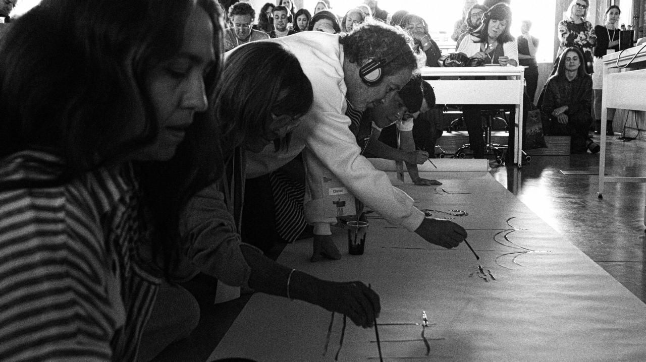Participantes de un taller pintan juntos sobre un papel en el piso, sin celulares