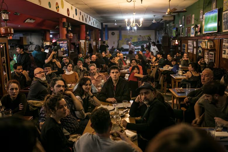 Un bar de barrio lleno de gente conversando en las mesas